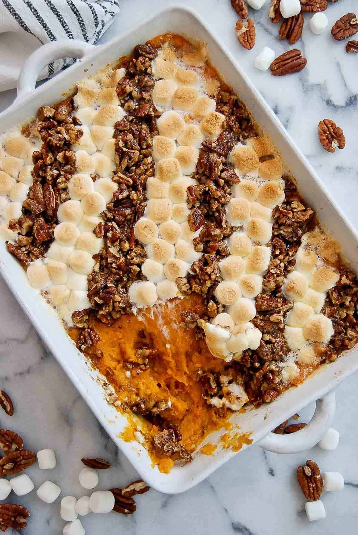 “Southern-style sweet potato casserole topped with toasted pecans and marshmallows in a yellow baking dish, served on a wooden table.”